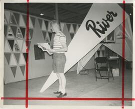 Man standing in front of big sign that says "River", no date.