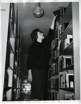 Women grabbing book from top shelf in the library stacks.