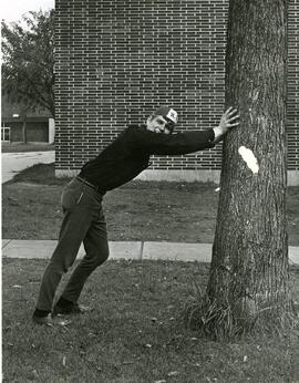 Student wearing freahsman beanie leaning on tree, 1950-1970.