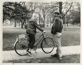 student on bike talking to student on sidewalk