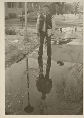 Student walking over a puddle on the sidewalk, 1977.