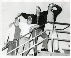 Students on stairs holding beanies on heads, 1964