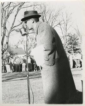 Person speaking into a microphone to a big group, no date.